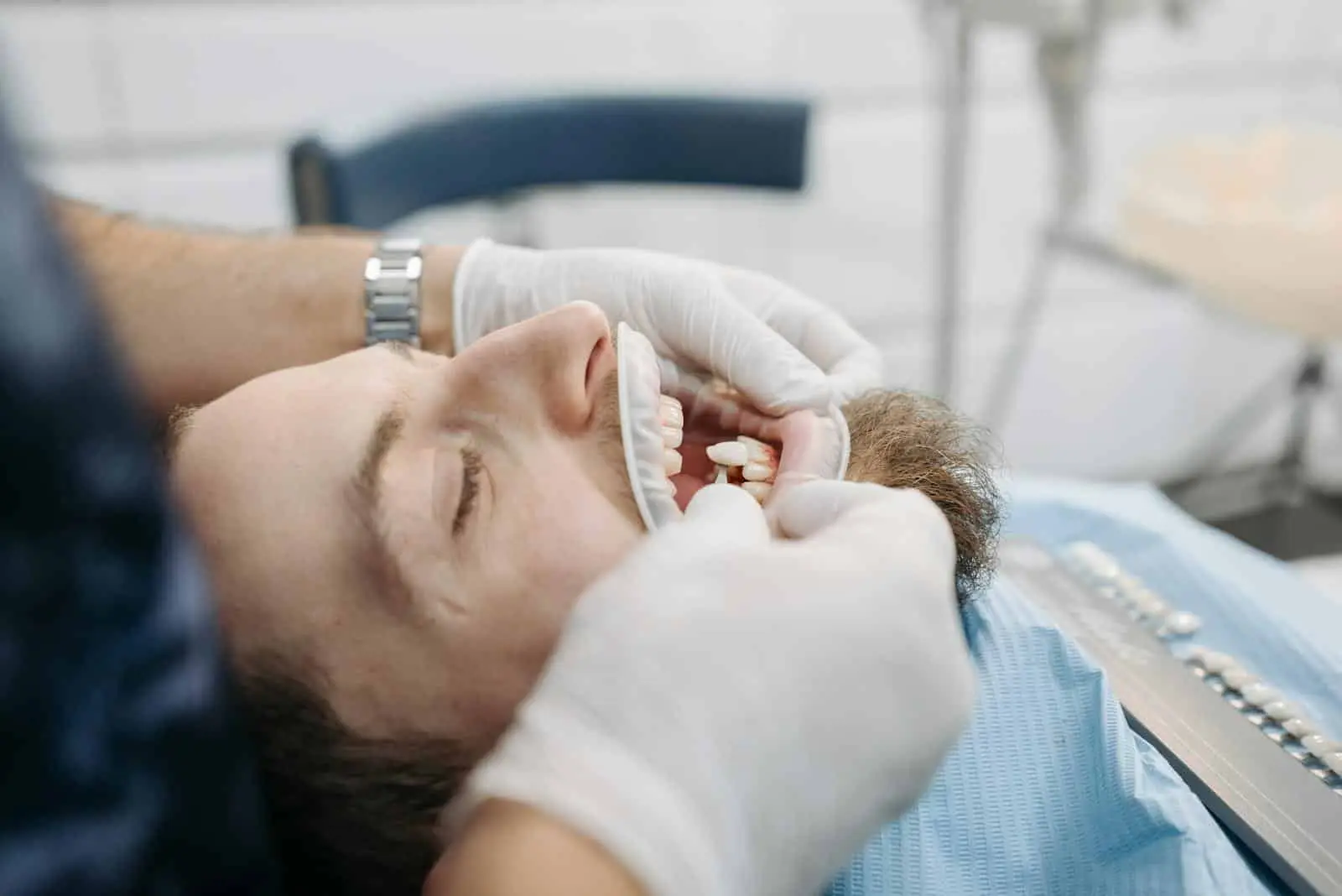 Dentist using shade guide to match patient's teeth color in dental clinic.
